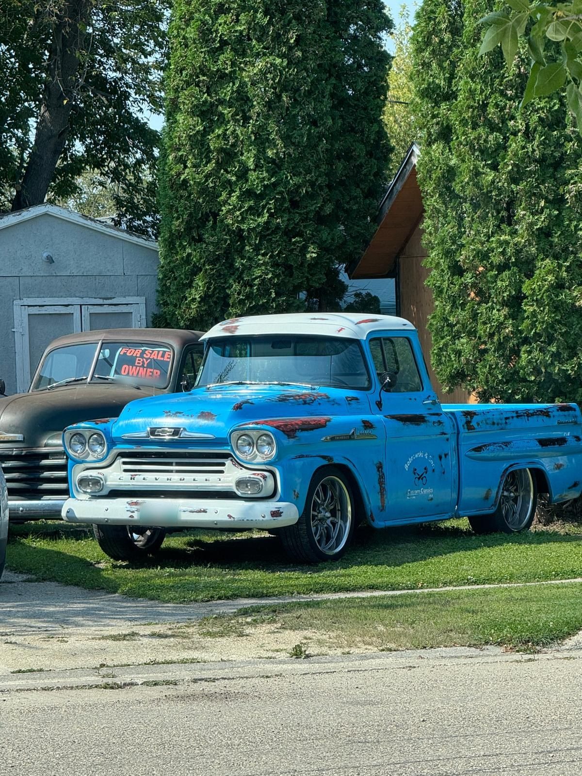 Blue pickup with white roof and worn paint showing red primer, on polished wheels
