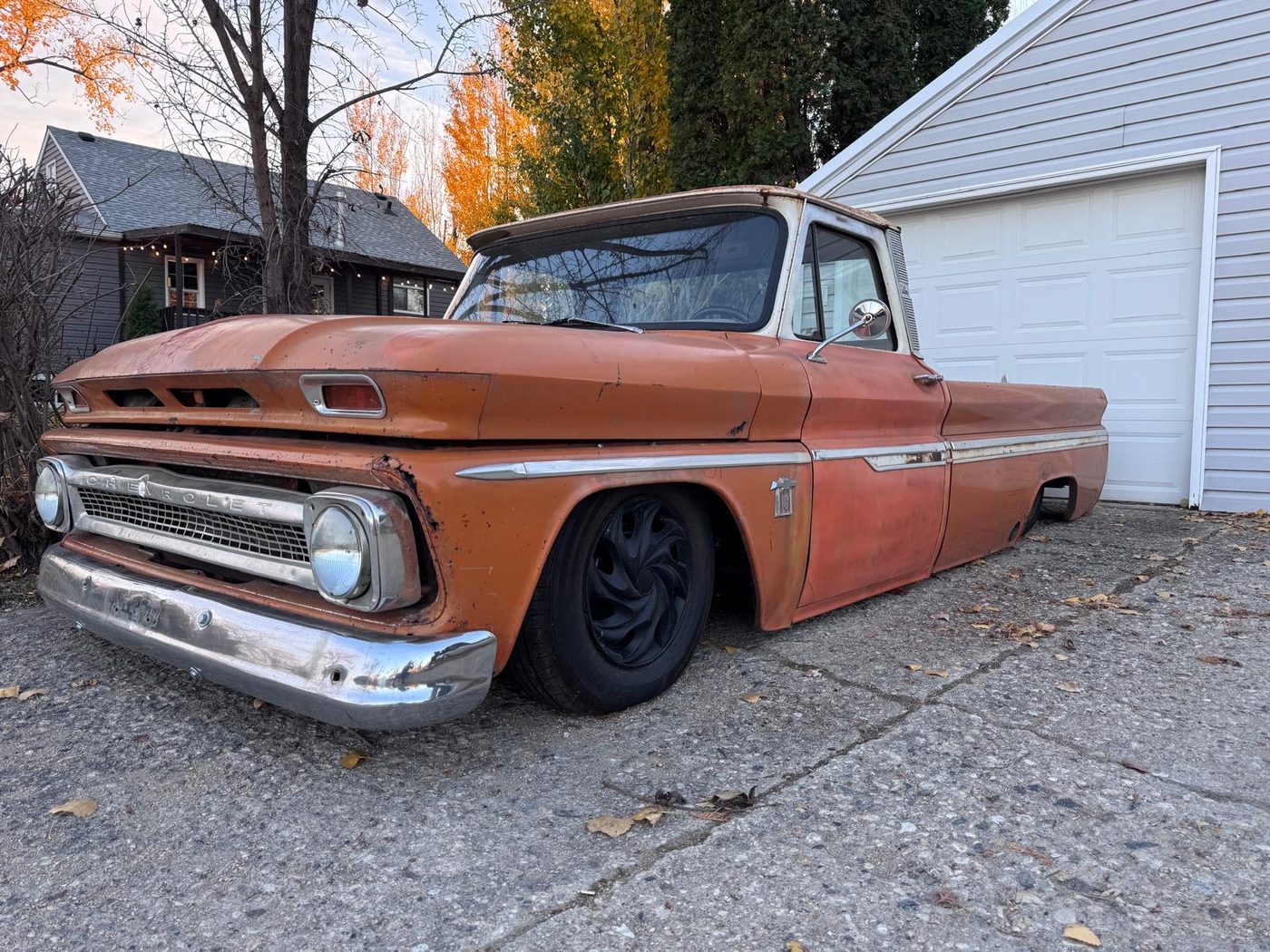 Front three-quarter view of the 1965 Chevrolet C10 with white roof, parked by a garage