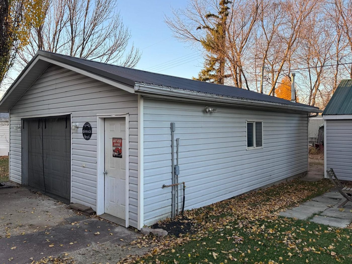 Red River Rod & Custom Inc. shop: a white-sided building with a dark steel roof and a single bay door, autumn leaves on the lawn