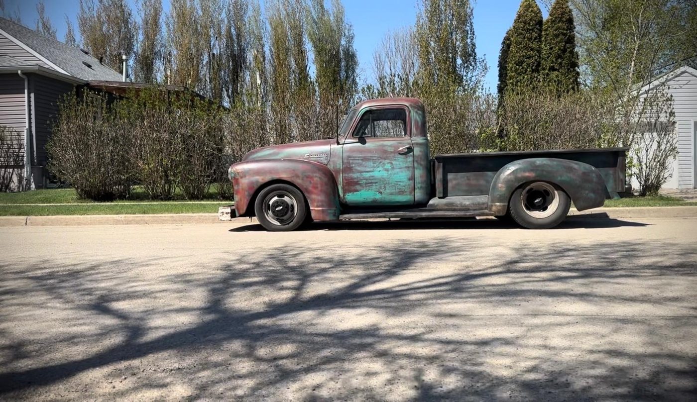 Side profile of a weathered turquoise and red classic pickup, lowered on black steel wheels